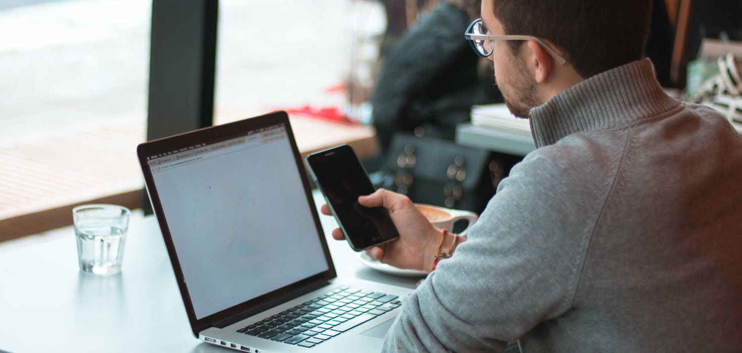 Man with cell phone in front of laptop