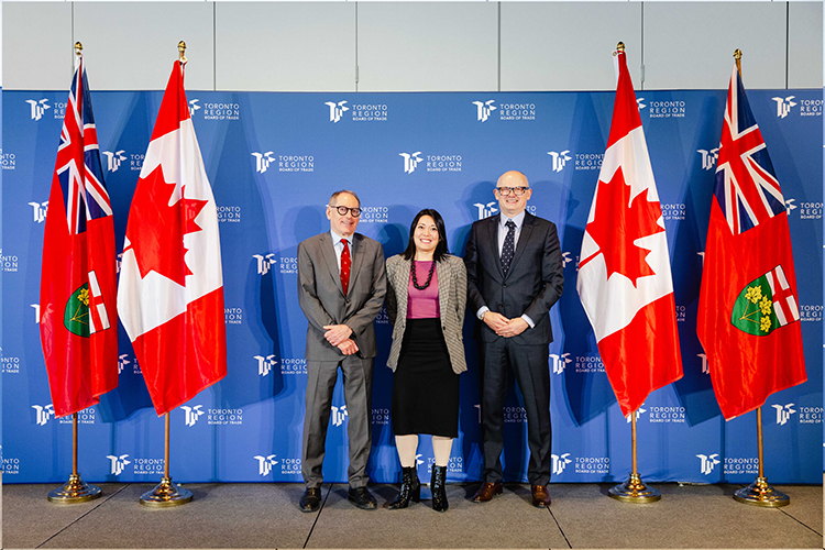 Three people stand in front of Canadian and Ontario flags