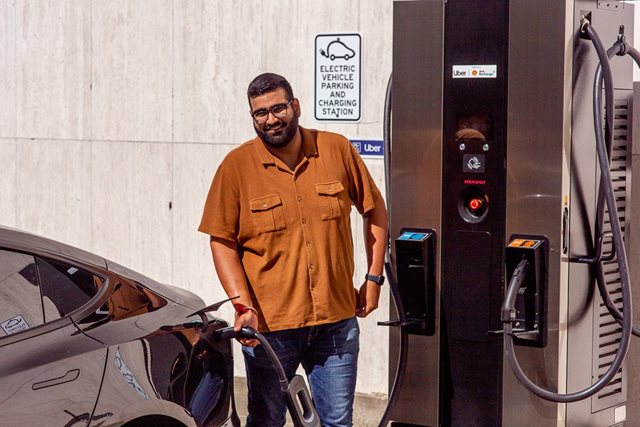 A man smiling, while charging his electric vehicle.