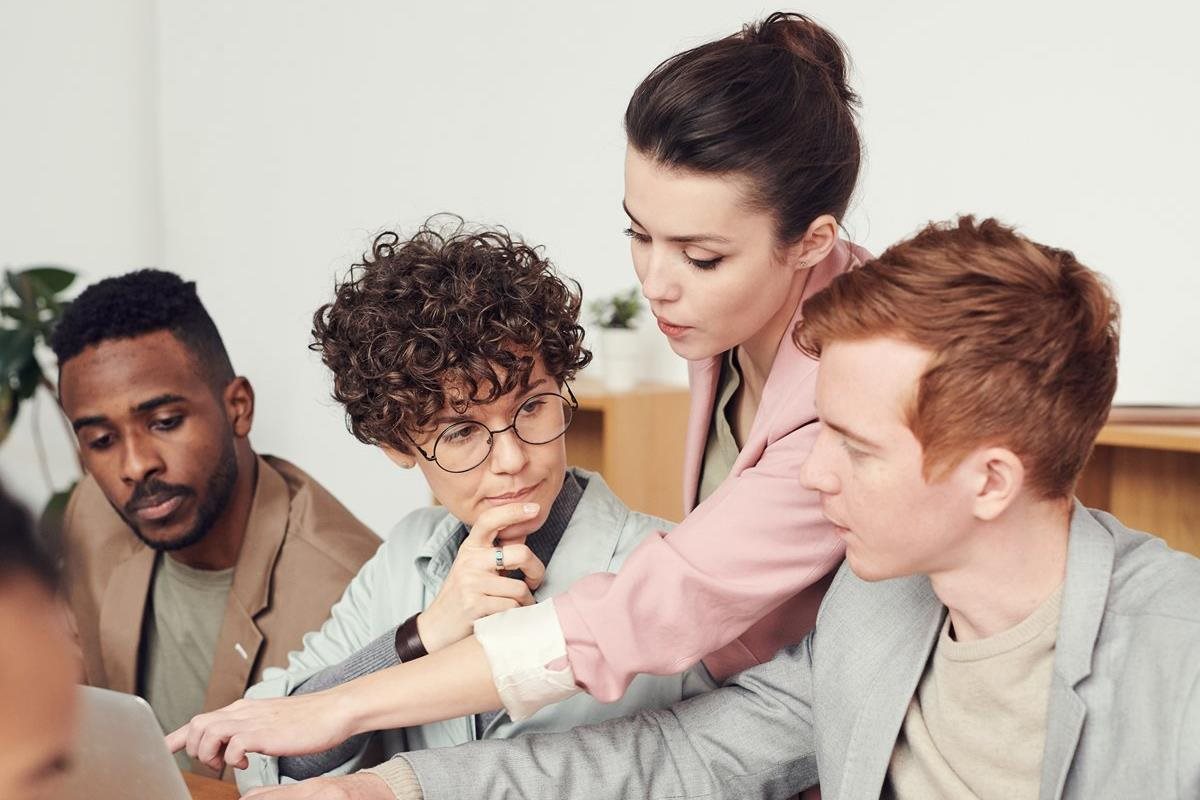 A woman helps a man with something on their workscreen in a meeting.