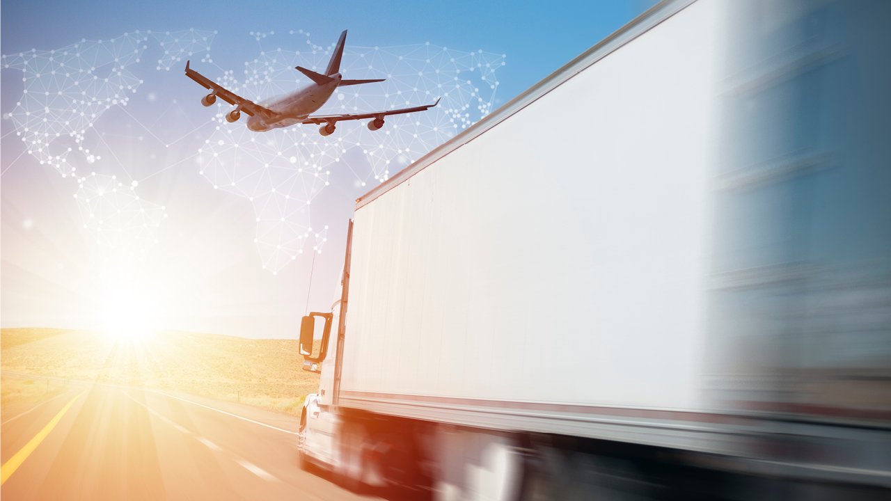 A freight truck drives on a sunny highway, a plane flies overhead