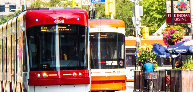 Two street cars pass by a cyclist on a sunny day.