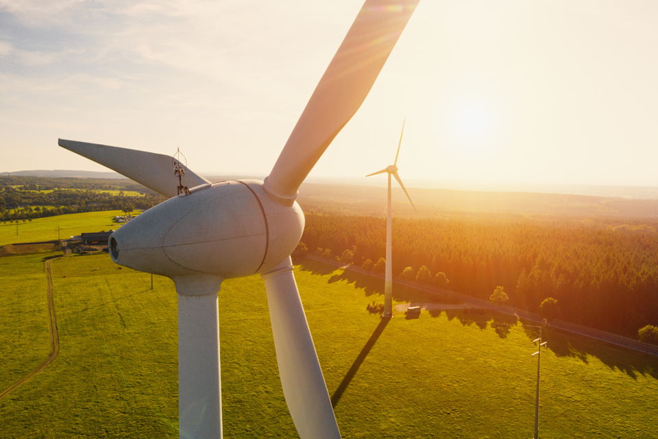 A close-up view of a wind turbine, positioned on a grassy field with the sun shining.