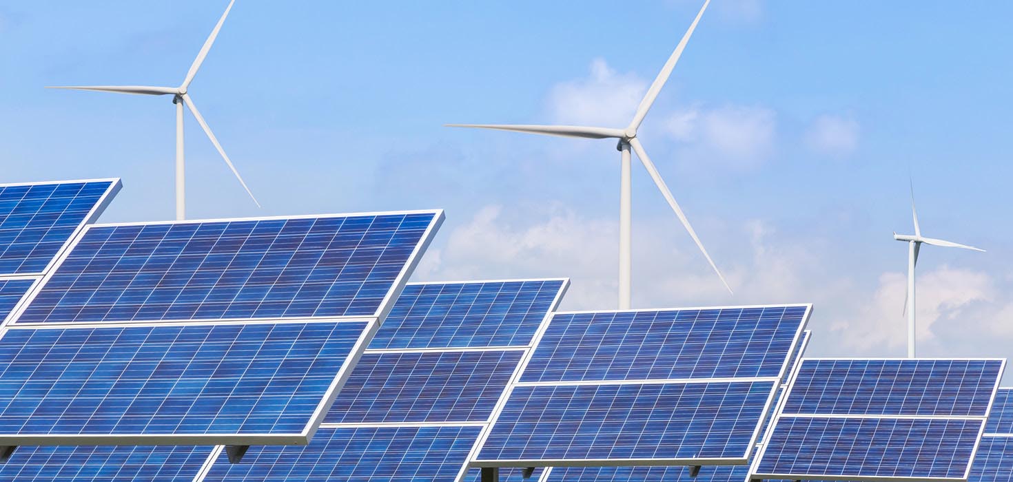 A field of solar panels with windmills in the distance.