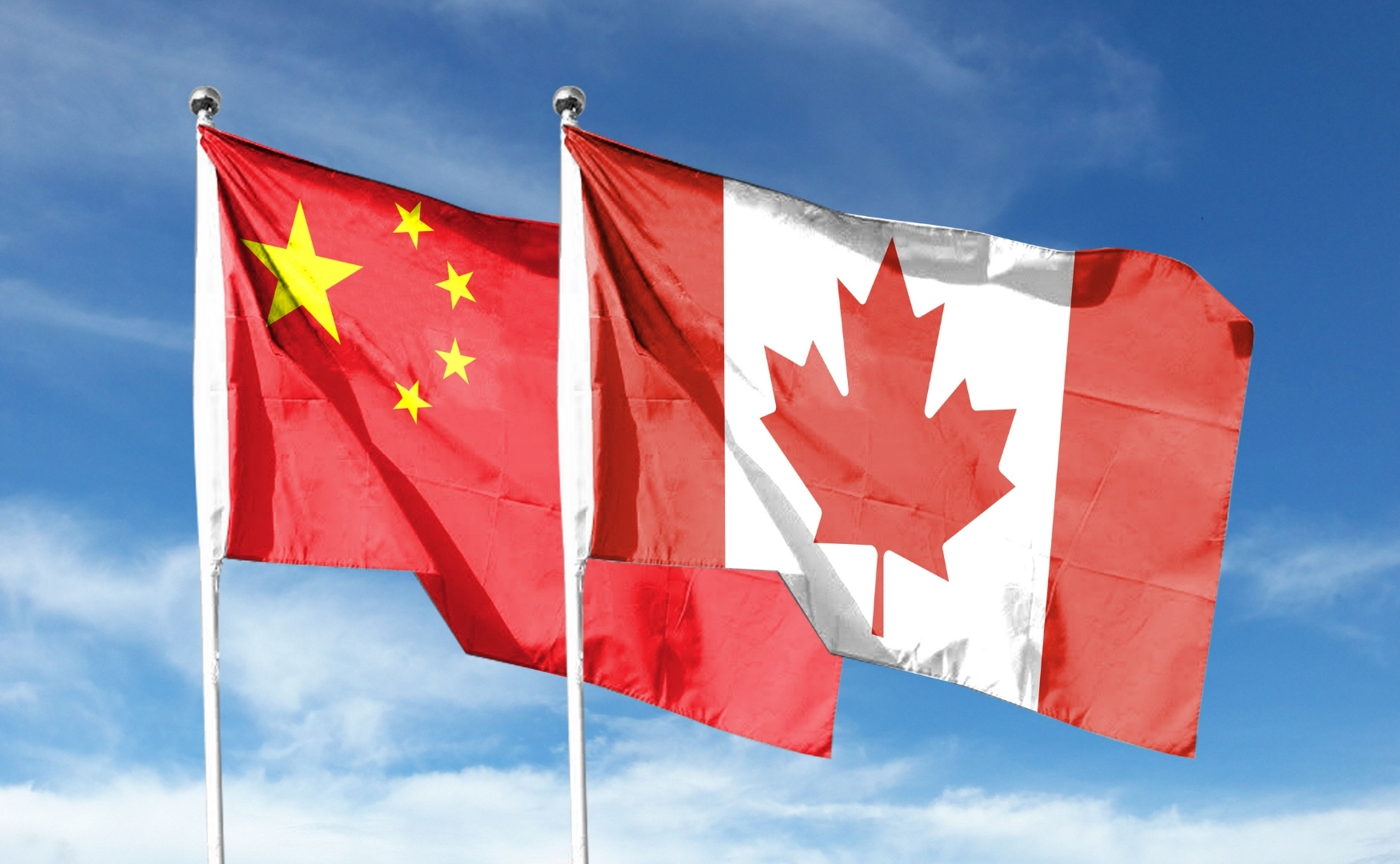 A Chinese and Canadian flag flying together against a blue sky