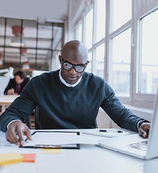 Man with glasses looking at documents and laptop