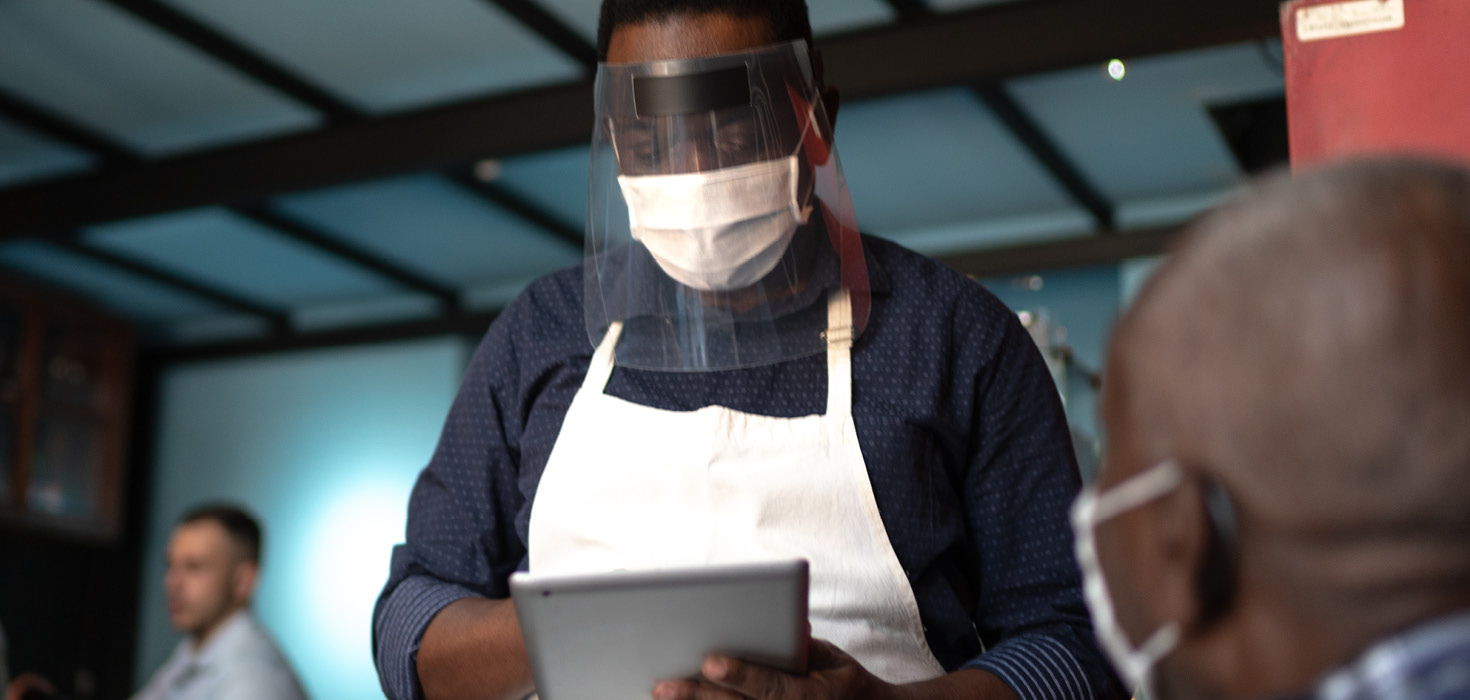 Restaurant employee in PPE and reviewing vaccine passports.