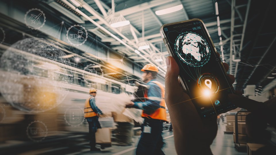 Worker in a warehouse holding a smartphone displaying a global logistics tracking interface, with digital supply chain icons overlaid in the background.