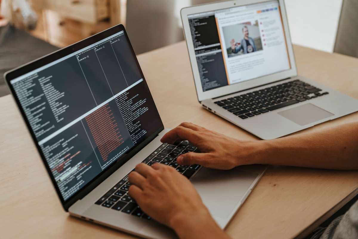 A person coding on a laptop while watching a video on another laptop.