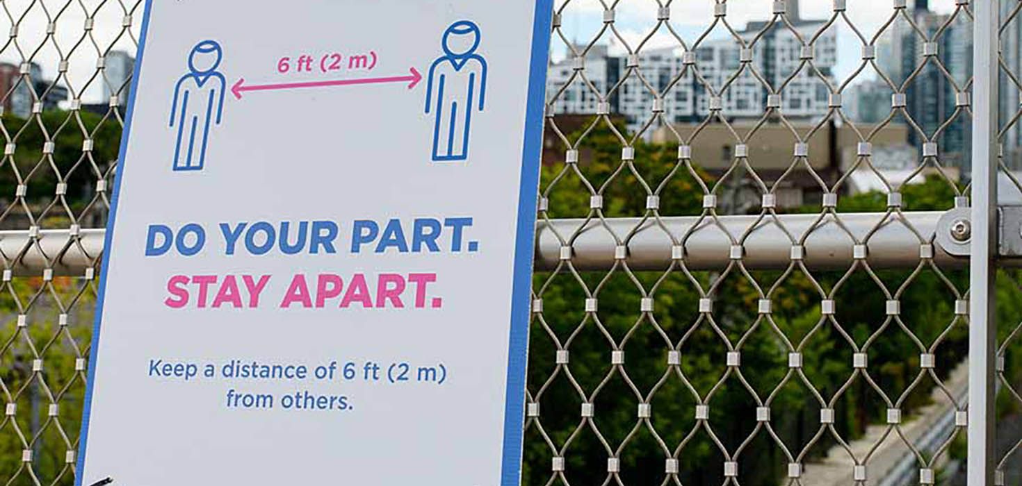 A sign that says, “Do your part. Stay apart,” is affixed to a chain-link fence. The Toronto skyline is in the background.