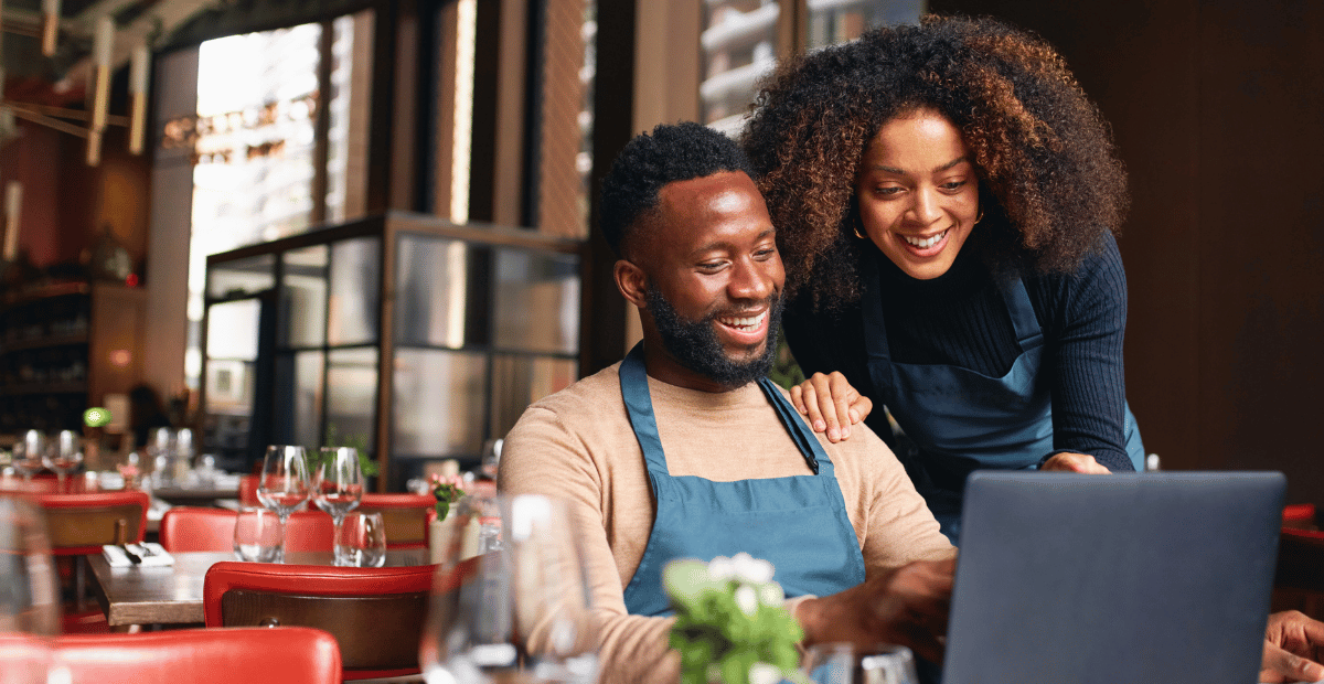 Two people working together on a computer at a restaurant.