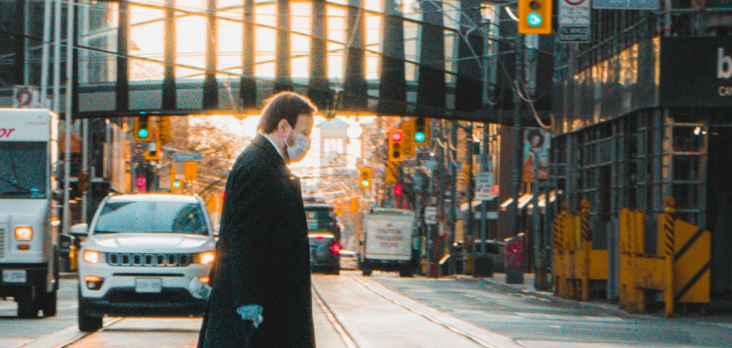 Masked man walking across a city street.